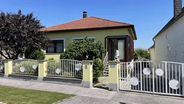 Gelbes Einfamilienhaus mit rotem Ziegeldach, Vorgarten und weißem Gartentor.