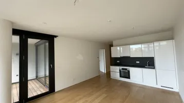 Heller offener Wohnbereich mit integrierter moderner Küche, Holzboden und Zugang zum Balkon.