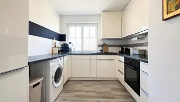Moderne Küche mit weißen Hochglanzfronten, dunkler Arbeitsplatte und Fenster mit Blick ins Grüne.