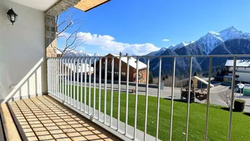 Heller Balkon mit Holzboden, modernem Geländer und beeindruckendem Bergblick.