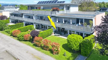 Luftaufnahme eines modernen Mehrfamilienhauses mit Solarpaneelen und gepflegter Gartenanlage.