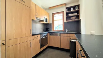Funktionale Küche mit Holzschränken, dunkler Arbeitsplatte und Fenster.
