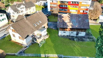 Luftaufnahme eines Wohngebiets mit mehreren Häusern, Gärten und einem bunten Mehrfamilienhaus.