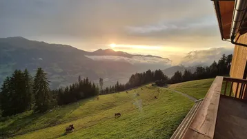 Sonnenuntergang über den Bergen, gesehen von einem Holzbalkon mit weitem Blick über das Tal.