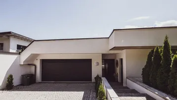 Moderne Hausfassade mit integrierter Garage und gepflastertem Eingangsbereich unter klarem Himmel.