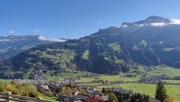 Panoramablick auf das Tal und die umliegenden Berge mit kleinen Dörfern unter blauem Himmel.