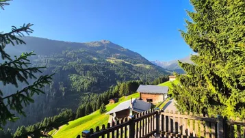 Malerische Berglandschaft mit traditionellen Holzhäusern und üppiger Vegetation unter blauem Himmel.