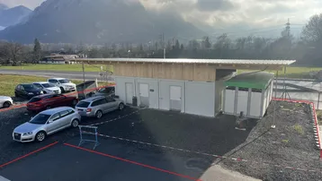 Außenansicht eines neuen modularen Gebäudes mit Parkplätzen und einer Bergkulisse im Hintergrund.