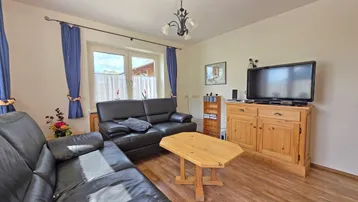 Gemütliches Wohnzimmer mit dunklen Ledersofas, Holzboden und Blick ins Grüne.