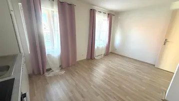 Helles, leeres Zimmer mit Laminatboden und zwei Fenstern, bereit zur individuellen Gestaltung.