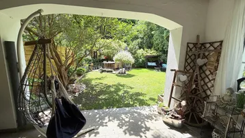 Überdachte Terrasse mit Hängesessel und Blick auf den grünen Garten mit Sitzbereich.