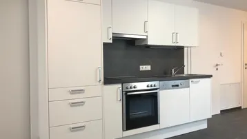Moderne Einbauküche in Weiß mit dunkler Arbeitsplatte und integrierten Geräten, bereit zur Nutzung.