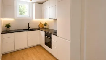 Moderne Einbauküche mit weißen Schränken, dunkler Arbeitsplatte und hellem Holzfußboden, gut beleuchtet.
