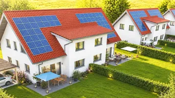 Moderne Einfamilienhäuser mit roten Dächern und Photovoltaikanlagen in grüner Landschaft.