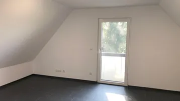 Heller Wohnraum mit Dachschrägen, Fliesenboden und Zugang zu einem französischen Balkon.