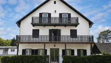 Traditionelles Wohnhaus mit weißer Fassade, schwarzen Fensterläden und mehreren Balkonen unter blauem Himmel.