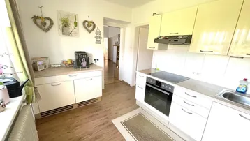 Helle Küche mit Laminatboden, weißen Schränken und Blick in den Flur.