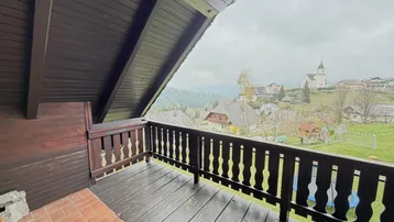 Rustikaler Holzbalkon mit weitem Blick über die Landschaft und ein Dorf mit Kirche.