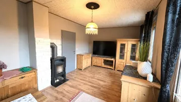 Wohnzimmer mit Holzboden, Kaminofen und rustikalen Holzmöbeln, gemütlich eingerichtet.