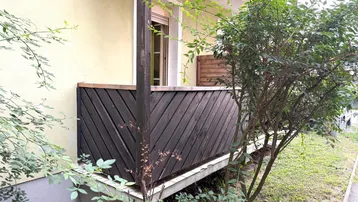 Kleiner Balkon mit Holzverkleidung und Blick ins Grüne, umgeben von Sträuchern.