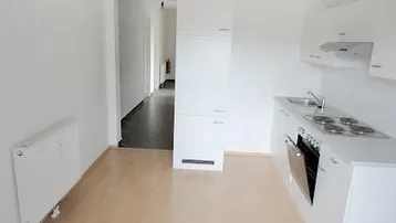 Kleine, funktionale Küche mit weißen Schränken, integrierten Geräten und hellem Laminatboden.