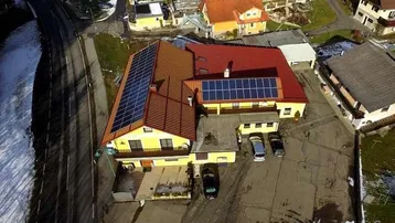 Luftaufnahme eines gelben Gebäudes mit rotem Dach, Solarpaneelen und Parkplatz in ländlicher Umgebung.