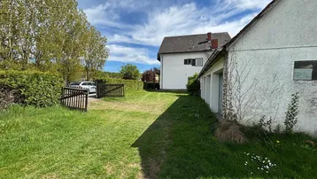 Blick auf das Grundstück mit Rasenfläche, Einfahrt und dem Hauptgebäude sowie einer Garage.