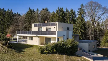 Modernes Wohnhaus mit Photovoltaikanlage auf dem Dach und großem Balkon in grüner Umgebung.