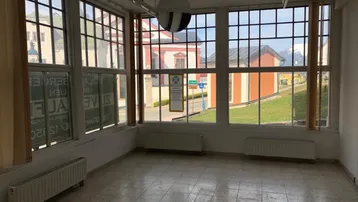 Heller Innenraum mit vielen Fenstern, Fliesenboden und weitem Blick auf die umliegende Landschaft.