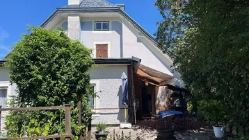 Seitenansicht des Hauses mit üppigem Grün und einem kleinen Gartenbereich unter blauem Himmel.