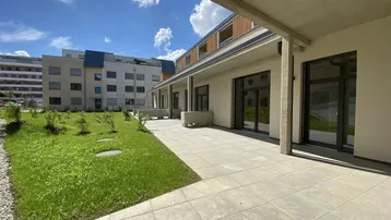 Moderne Terrasse mit angrenzender Rasenfläche und Blick auf das Gebäude unter blauem Himmel.