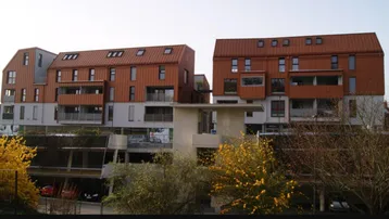Moderne Wohngebäude mit markanter kupferfarbener Fassade und Balkonen unter hellem Himmel.