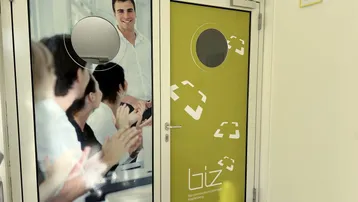 Eingangsbereich eines Bürogebäudes mit modernen Türen und Firmenbranding, das eine geschäftliche Atmosphäre vermittelt.