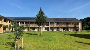 Moderne Wohnanlage mit Photovoltaikanlage auf dem Dach und großzügiger Grünfläche im Vordergrund.