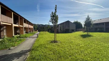 Moderne Wohngebäude mit Holzfassaden und Balkonen, umgeben von grünen Rasenflächen unter blauem Himmel.