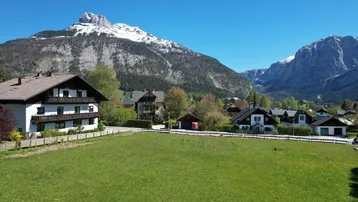 Blick auf eine ländliche Wohngegend mit traditionellen Häusern und schneebedeckten Bergen im Hintergrund.