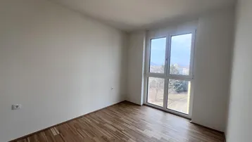 Helles Schlafzimmer mit Parkettboden und großem Fenster mit Blick ins Grüne.