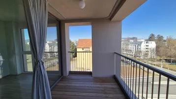 Geräumiger Balkon mit Holzboden und Blick auf die Stadt, ideal für entspannte Stunden im Freien.