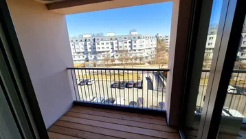 Heller Balkon mit Holzboden und Blick auf die umliegenden Wohngebäude und den Parkplatz.