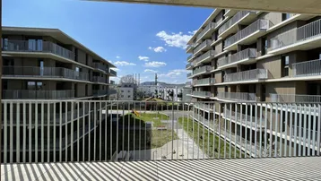 Blick vom Balkon auf den begrünten Innenhof und die modernen Wohngebäude der Anlage.