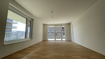 Helles, leeres Zimmer mit Parkettboden und Zugang zu einem französischen Balkon.