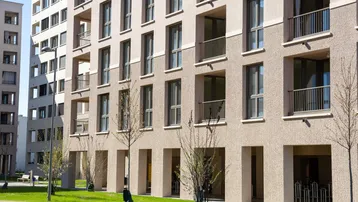 Moderne Wohngebäude-Fassade mit Balkonen, großen Fenstern und begrüntem Außenbereich im Sonnenlicht.