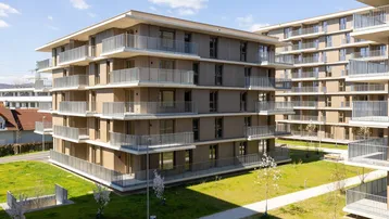 Moderne Wohngebäude mit Holzfassaden und zahlreichen Balkonen in einer grünen Umgebung.