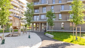 Moderner Wohnkomplex mit Holzfassade und einem Spielplatz mit Sandfläche für Kinder.