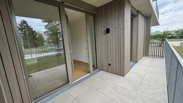 Geräumiger Balkon mit Fliesenboden und Holzverkleidung, bietet Zugang zu einem hellen Innenraum.