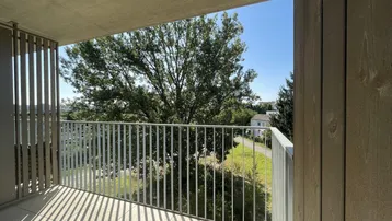 Geräumiger Balkon mit Fliesenboden, Metallgeländer und Blick ins Grüne unter blauem Himmel.
