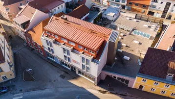 Luftaufnahme eines modernen Gebäudekomplexes mit rotem Dach, umgeben von älteren Stadtgebäuden.