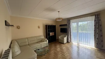 Helles Wohnzimmer mit Fischgrätparkett, beigem Ecksofa und Zugang zum Balkon.