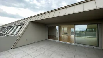 Geräumige Dachterrasse mit modernen Fliesen, Schiebetüren und weitem Blick über die Stadt.