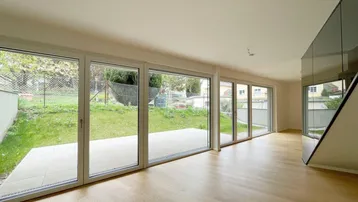 Helles Wohnzimmer mit großen Fensterfronten und direktem Zugang zur Terrasse und Garten.